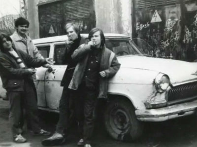 Teenagers with cigarettes pose against the background of an old car “Volga” 80s
